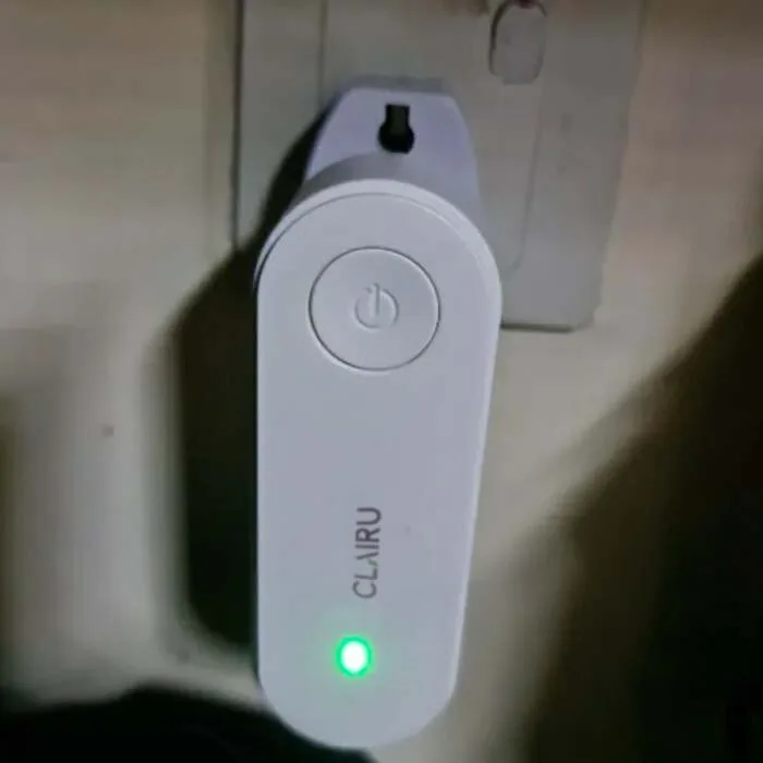 Clairu air purifier glowing with its green indicator light while plugged into a wall socket