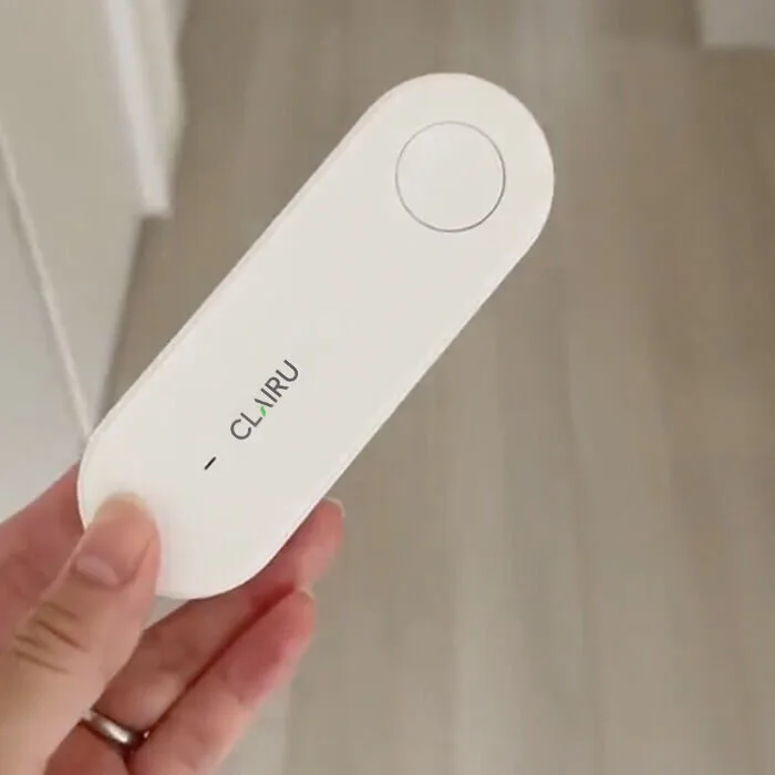 Clairu air purifier held in a hand to show its palm-sized oval body and round power button
