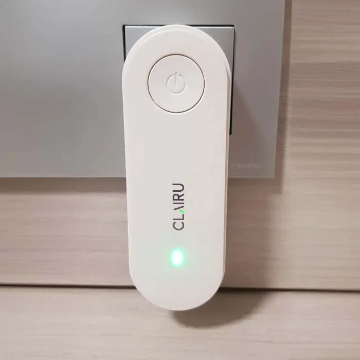 Clairu unit plugged into a wall socket on a wooden panel wall with its green light on
