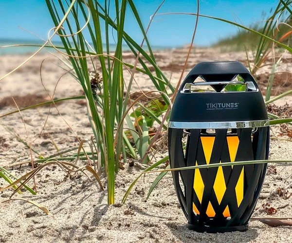 TikiTunes on a sandy beach with dune grass, showing the tiki torch design in natural outdoor light