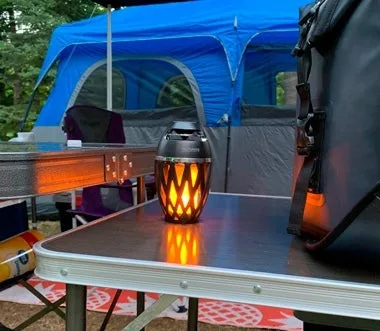 TikiTunes glowing on a camping table next to a blue tent and gear bag